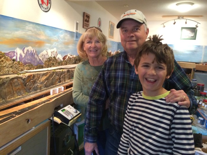 Lynda and Dave with Charlie next to Dave's model trains in their basement