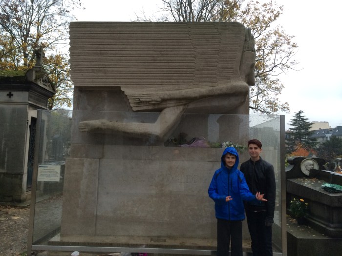 Charlie inexplicably plays air bass at Oscar Wilde's grave. Wilde, who died of meningitis in 1900 after two years of prison and hard labor leading to poor health, had recently been exiled and was estranged from his wife and children. An anonymous donor paid for his tomb which a friend designed. So many female mourners have kissed the tomb that there are lipstick marks on the side of it, and a barrier has been erected to prevent further damage.